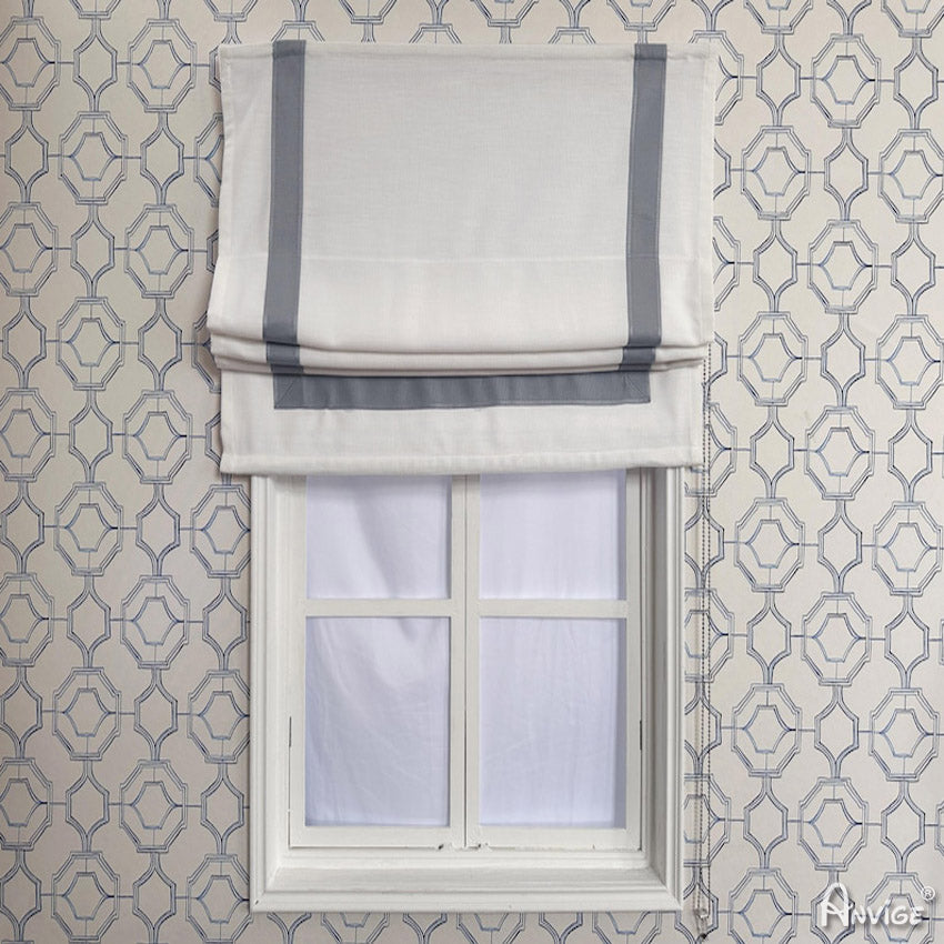 Anvige Flat Roman Shades in white with gray trim, installed on a window with geometric wallpaper. Light-filtering and custom-sized.