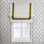 Flat Roman shades in white with mustard yellow trim, mounted on a window with geometric wallpaper. Customizable light-filtering blinds.