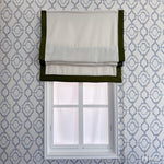 Flat Roman shade with white fabric and green border, mounted on a window with geometric wallpaper. Customizable light-filtering window treatment.