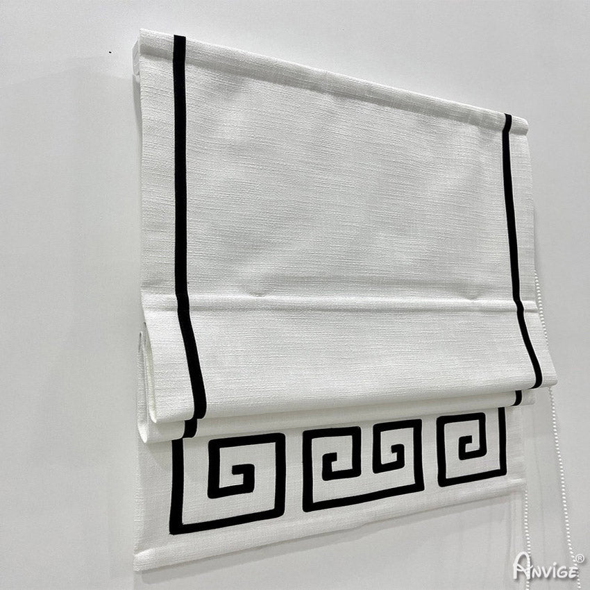 Close-up of white flat Roman shades with black geometric border, showcasing sleek design and pull cord mechanism. Ideal for custom window treatments.