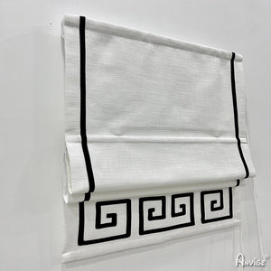 Close-up of white flat Roman shades with black geometric border, showcasing sleek design and pull cord mechanism. Ideal for custom window treatments.