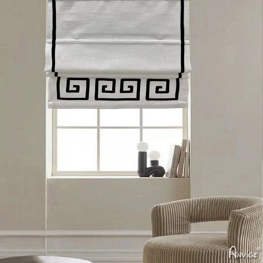 Flat Roman shades with black geometric border design, mounted on a window in a modern living room. Customizable and easy to install.