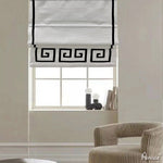 Flat Roman shades with black geometric border design, mounted on a window in a modern living room. Customizable and easy to install.