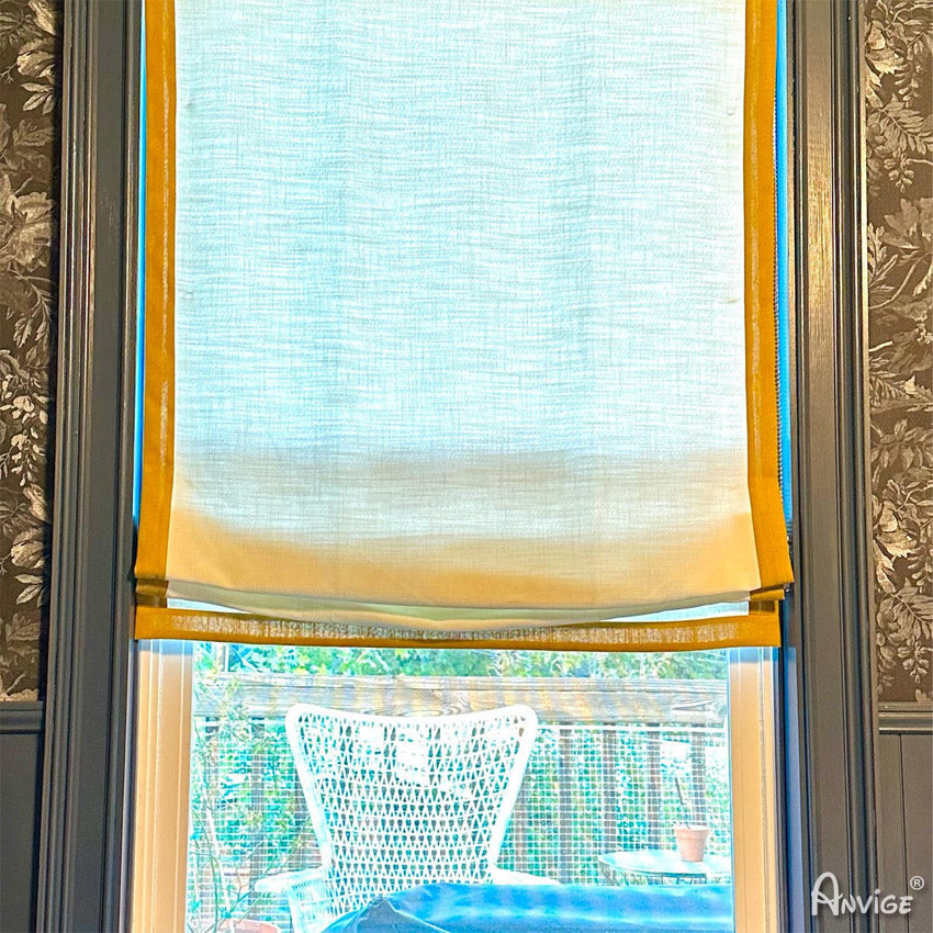 Anvige custom flat roman shade in light fabric with yellow border, installed on a window, providing light filtering and privacy.