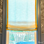 Anvige custom flat roman shade in light fabric with yellow border, installed on a window, providing light filtering and privacy.