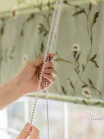 Hand operating the chain mechanism of a green floral Roman shade, demonstrating its smooth functionality and ease of use.