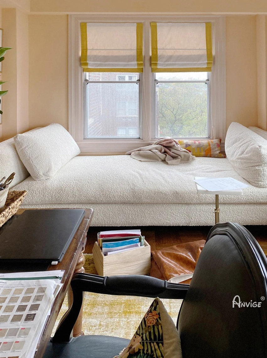 Anvige flat Roman shades in white with yellow border trims, installed on two windows in a cozy living space with a white daybed and desk.